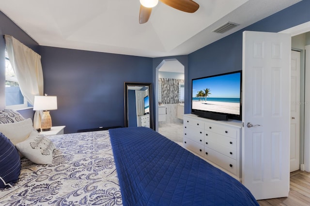 bedroom featuring ensuite bath, arched walkways, a ceiling fan, wood finished floors, and visible vents