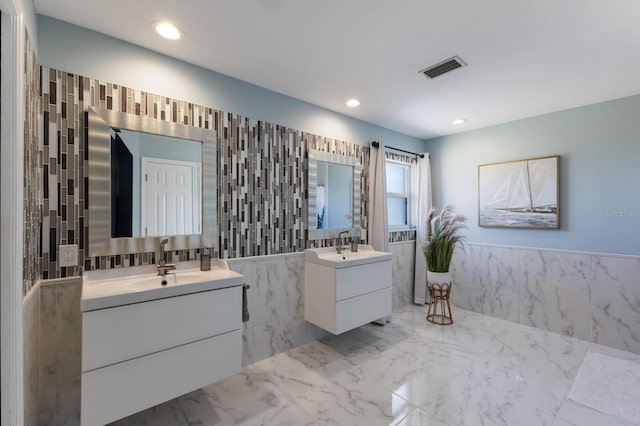 full bath featuring visible vents, marble finish floor, two vanities, and tile walls