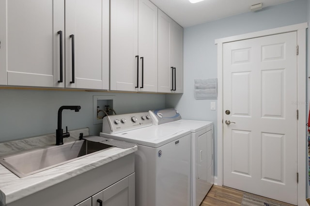 laundry area featuring independent washer and dryer, light wood-style floors, a sink, and cabinet space