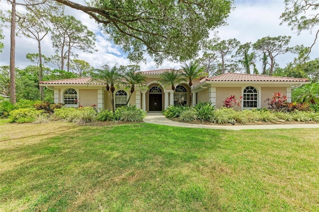 mediterranean / spanish-style house with a tiled roof, a front yard, and stucco siding
