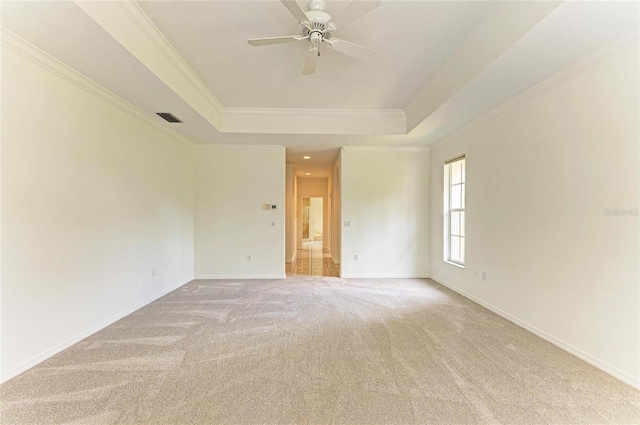 unfurnished room featuring a ceiling fan, visible vents, light colored carpet, ornamental molding, and a tray ceiling