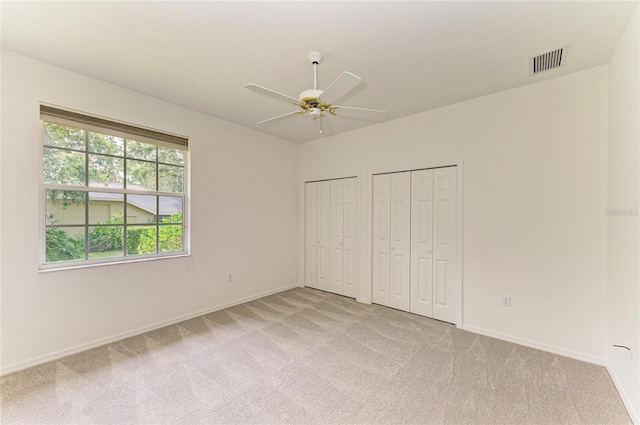 unfurnished bedroom with multiple closets, visible vents, light carpet, and baseboards
