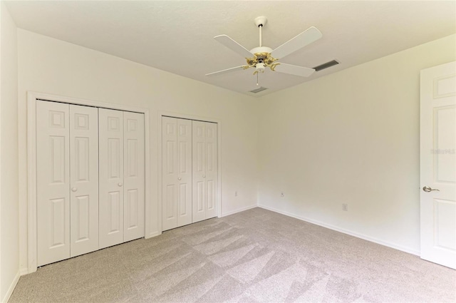 unfurnished bedroom with ceiling fan, multiple closets, carpet, baseboards, and visible vents