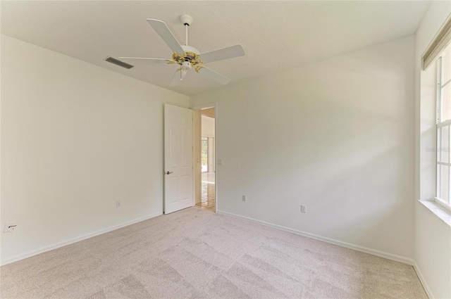 empty room featuring light colored carpet, baseboards, ceiling fan, and visible vents