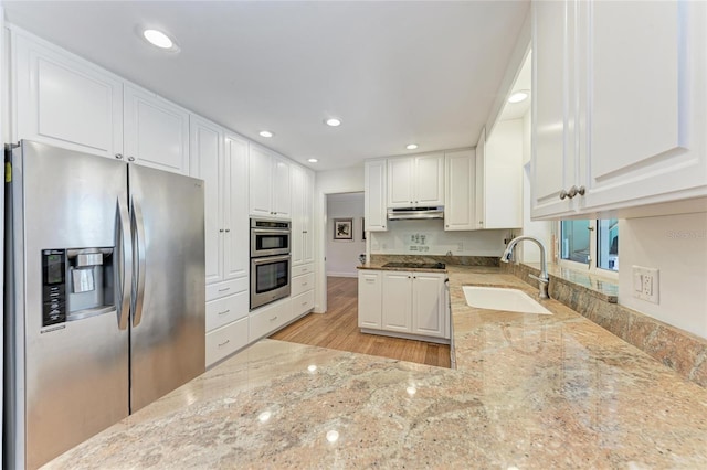 kitchen featuring stainless steel appliances, light stone countertops, under cabinet range hood, and a sink