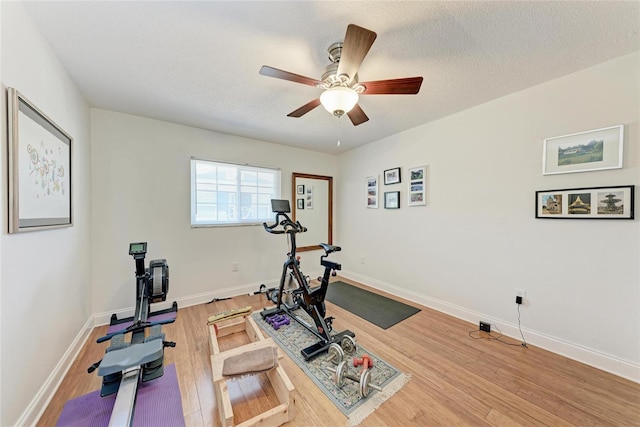 exercise room with light wood finished floors, a ceiling fan, a textured ceiling, and baseboards