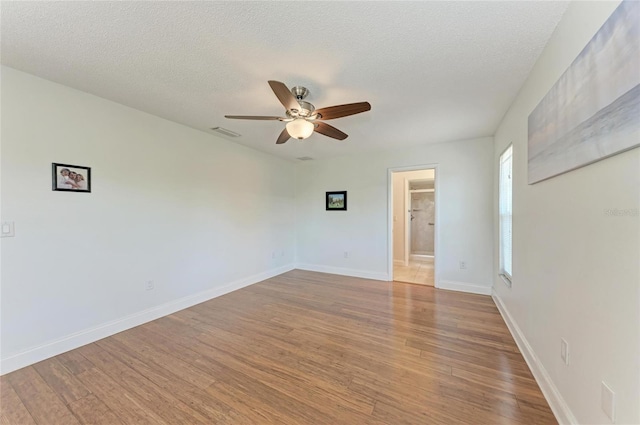 unfurnished room featuring wood finished floors, baseboards, visible vents, a ceiling fan, and a textured ceiling