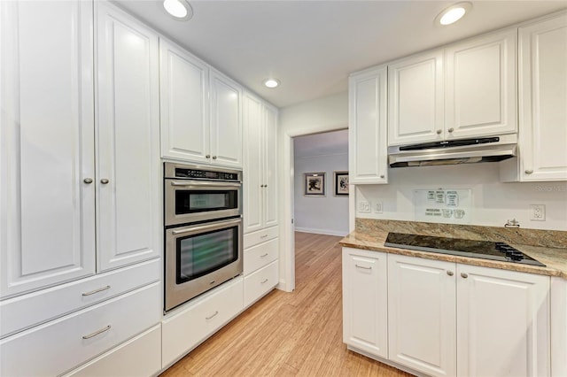 kitchen featuring white cabinets, light wood-style flooring, under cabinet range hood, stainless steel double oven, and black electric cooktop