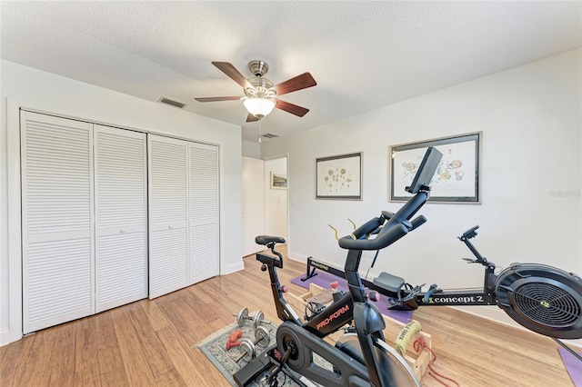 exercise area featuring light wood-type flooring, visible vents, a ceiling fan, and baseboards