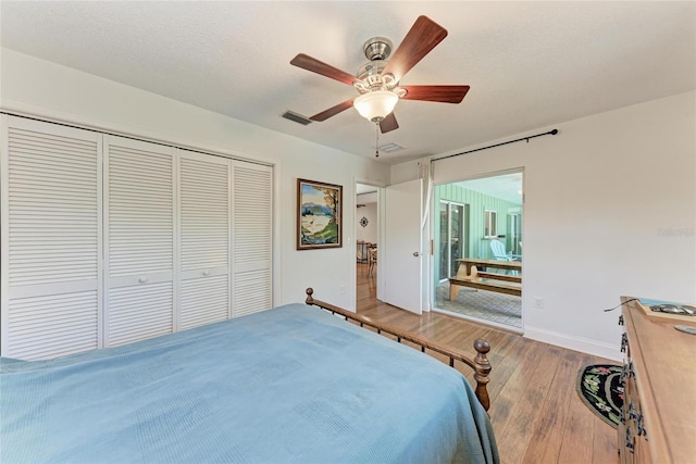 bedroom featuring wood finished floors, a closet, ceiling fan, baseboards, and visible vents