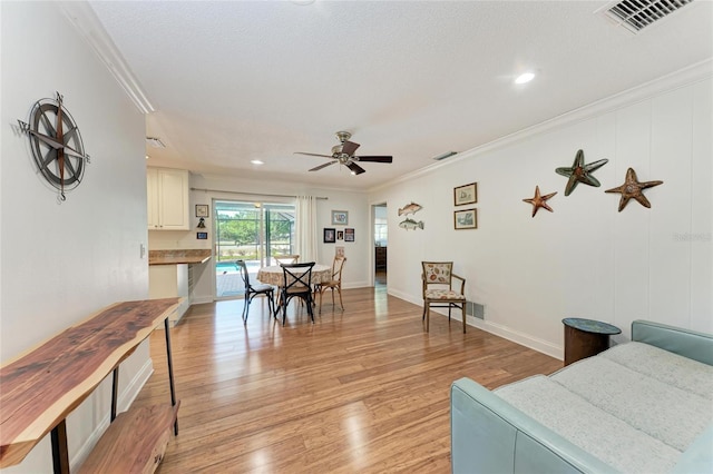 living area featuring crown molding, light wood finished floors, a ceiling fan, and visible vents