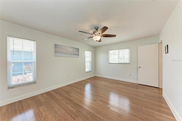 unfurnished room with a textured ceiling, a ceiling fan, light wood finished floors, and baseboards