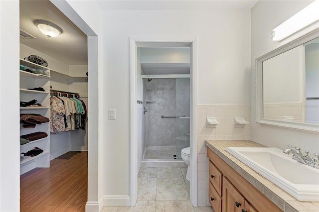 bathroom with tile patterned flooring, a shower stall, toilet, vanity, and a spacious closet