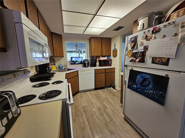 kitchen with light countertops, visible vents, a sink, white appliances, and brown cabinetry