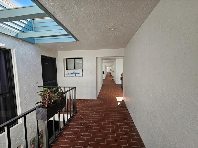 corridor featuring a textured wall, a textured ceiling, brick floor, and a skylight