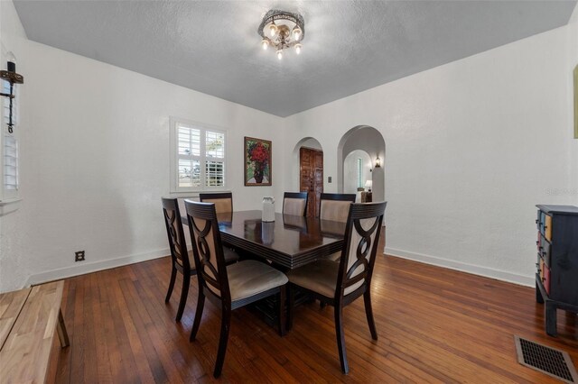 dining space with a textured ceiling, visible vents, arched walkways, hardwood / wood-style flooring, and baseboards