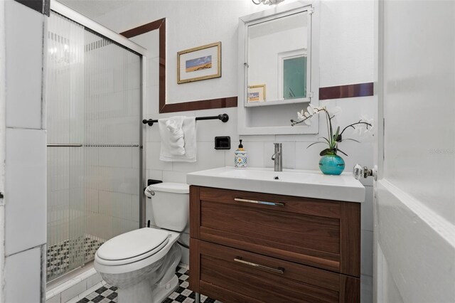 bathroom with vanity, toilet, tile walls, a wainscoted wall, and a stall shower