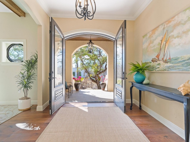entryway with ornamental molding, a notable chandelier, wood finished floors, and baseboards