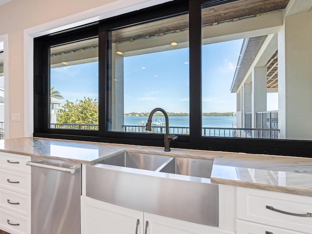 kitchen featuring light stone countertops, a water view, dishwasher, a sink, and white cabinetry
