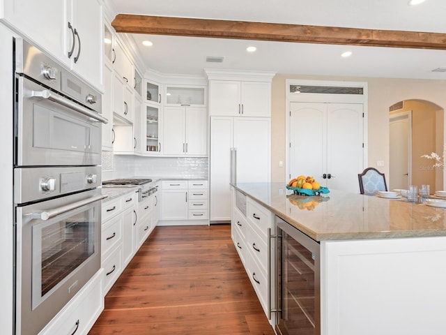 kitchen featuring arched walkways, beam ceiling, appliances with stainless steel finishes, and beverage cooler