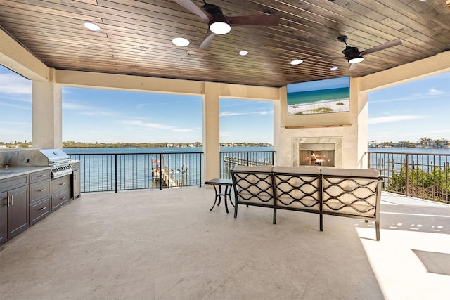 view of patio with a water view, an outdoor living space with a fireplace, exterior kitchen, a ceiling fan, and grilling area