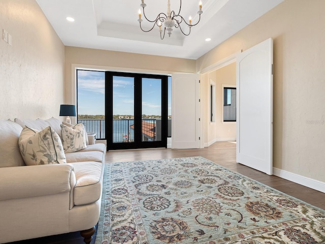 living room featuring recessed lighting, wood finished floors, baseboards, a notable chandelier, and a tray ceiling