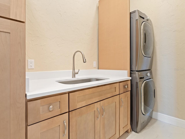 laundry room featuring stacked washer and clothes dryer, cabinet space, a textured wall, and a sink
