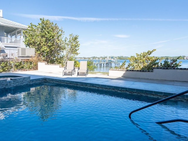 view of swimming pool with a patio area, a water view, and a pool with connected hot tub