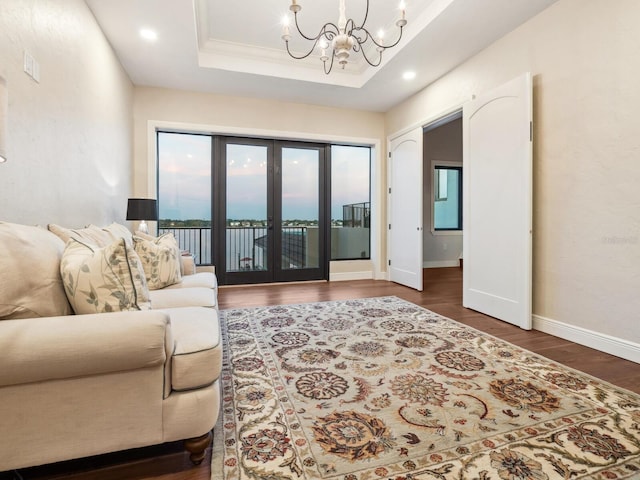 living area with a raised ceiling, a chandelier, baseboards, recessed lighting, and wood finished floors