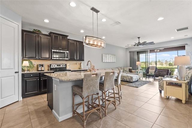 kitchen with visible vents, a sink, light stone counters, open floor plan, and stainless steel appliances