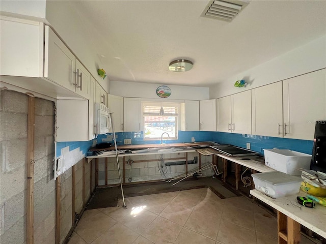 kitchen featuring white cabinetry, visible vents, light tile patterned floors, and white microwave