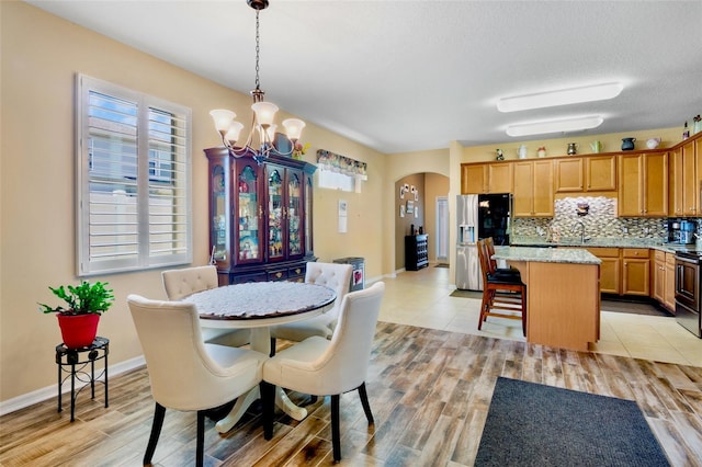 dining area featuring an inviting chandelier, baseboards, light wood finished floors, and arched walkways