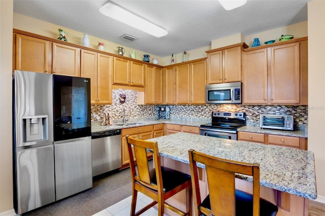 kitchen with a toaster, stainless steel appliances, a sink, visible vents, and a kitchen breakfast bar