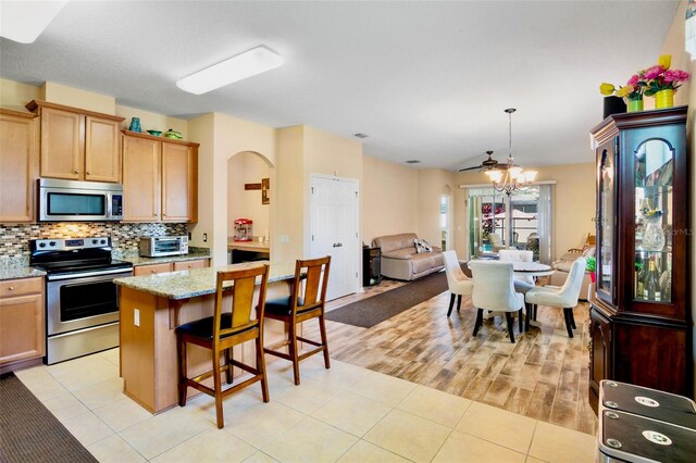 kitchen with appliances with stainless steel finishes, a breakfast bar, a chandelier, open floor plan, and backsplash