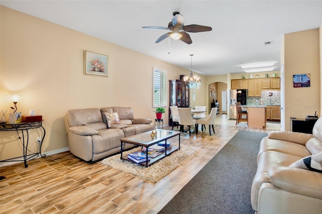 living room featuring visible vents, light wood-style floors, baseboards, arched walkways, and ceiling fan with notable chandelier