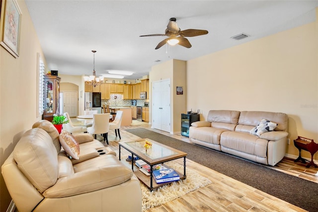 living room with light wood-style floors, visible vents, baseboards, arched walkways, and ceiling fan with notable chandelier