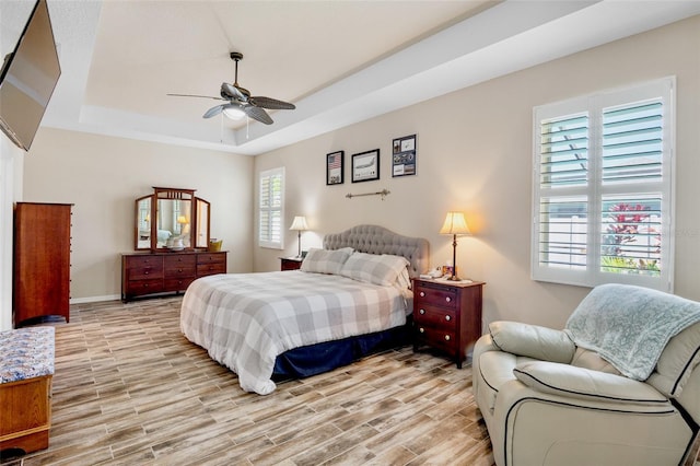 bedroom with baseboards, ceiling fan, light wood finished floors, and a tray ceiling