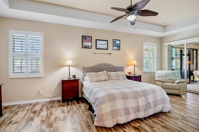 bedroom featuring wood finished floors, a raised ceiling, baseboards, and multiple windows