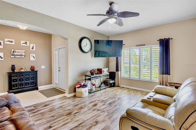 living room featuring arched walkways, a ceiling fan, wood finished floors, and baseboards
