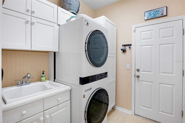 clothes washing area with a sink, cabinet space, light tile patterned floors, baseboards, and stacked washer and dryer