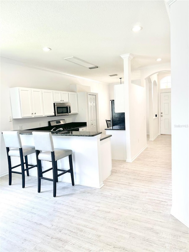 14315 Tree Swallow Way, Lakewood Ranch, FL 34202 - kitchen with stainless steel microwave, white cabinets, light wood-type flooring, arched walkways, and recessed lighting