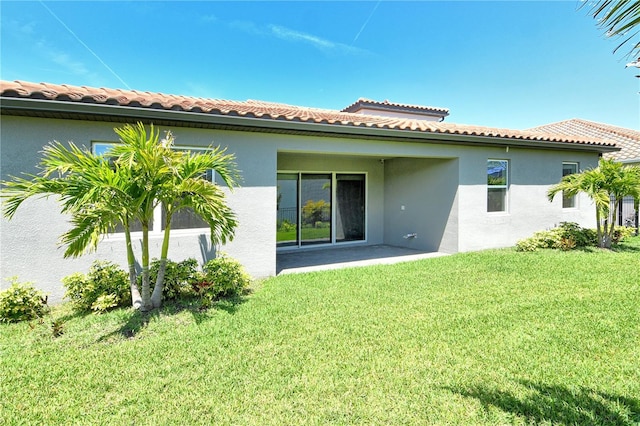rear view of house featuring a tiled roof, stucco siding, a yard, and a patio