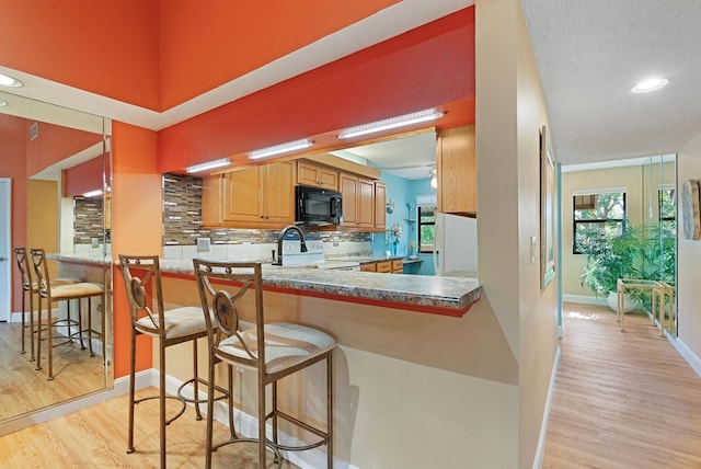 5736 Ashton Lake Dr, Sarasota, FL 34231 - kitchen featuring black microwave, range, light wood-type flooring, backsplash, and a breakfast bar area
