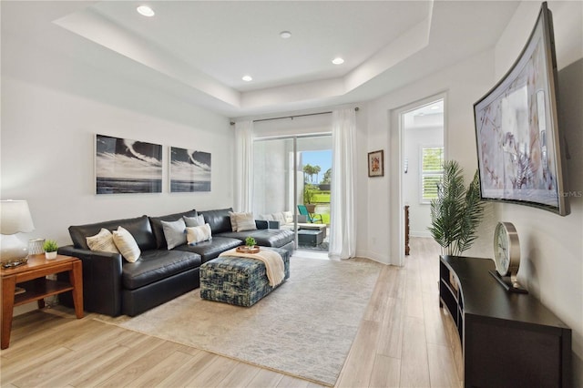 living area with a raised ceiling, light wood-style flooring, recessed lighting, and baseboards