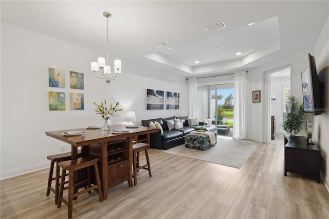 dining area featuring a raised ceiling, light wood-style floors, a chandelier, recessed lighting, and baseboards