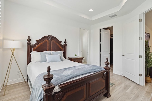 bedroom with light wood-style flooring, a tray ceiling, baseboards, and recessed lighting