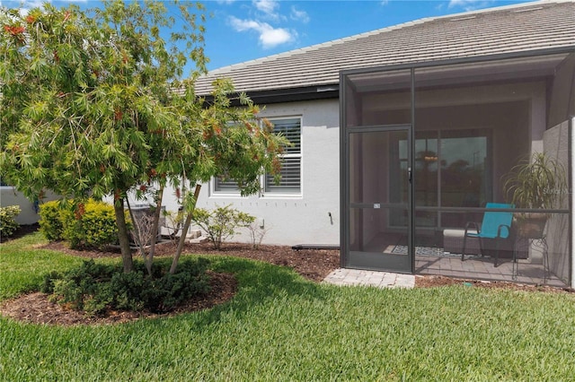 back of house featuring a sunroom, a lawn, a tiled roof, and stucco siding
