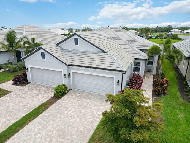 view of front of house with decorative driveway, a tiled roof, stucco siding, a garage, and a front yard