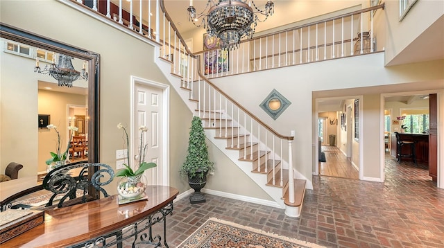 foyer entrance featuring stairs, brick floor, a high ceiling, and a notable chandelier