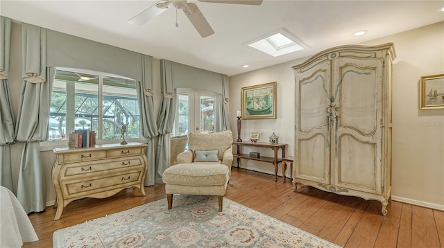 sitting room featuring ceiling fan, hardwood / wood-style floors, a skylight, and a healthy amount of sunlight